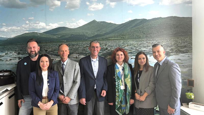 Seven people smiling in business attire, standing in front of a mountain landscape mural.